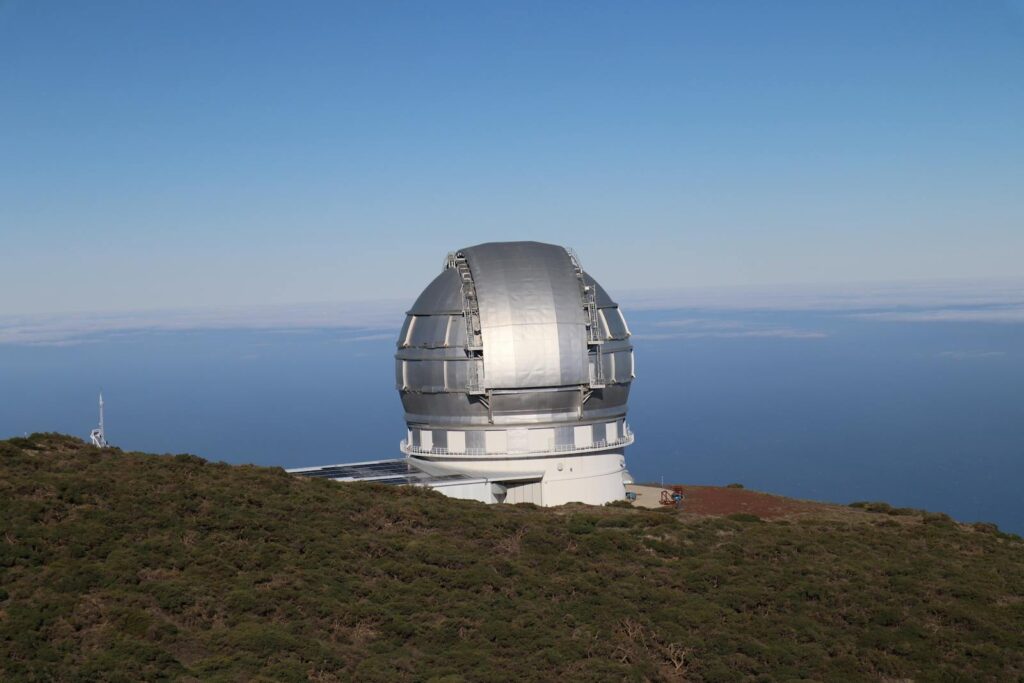 A contemporary observatory on a hillside, with ocean views under a clear sky.