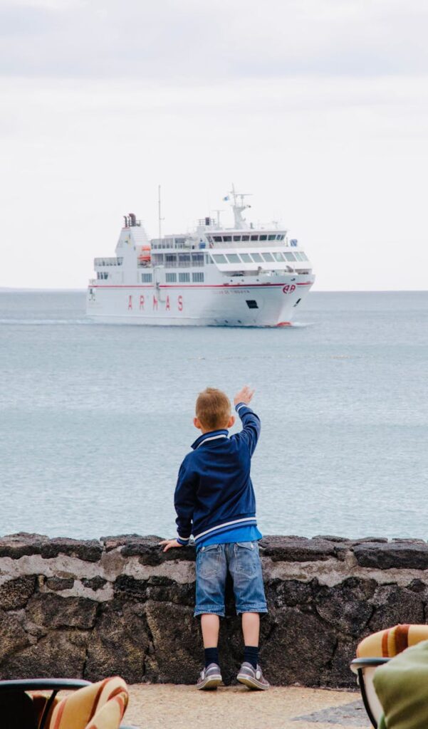 A young boy points towards a ship on the Lanzarote coastline, capturing curiosity and adventure.