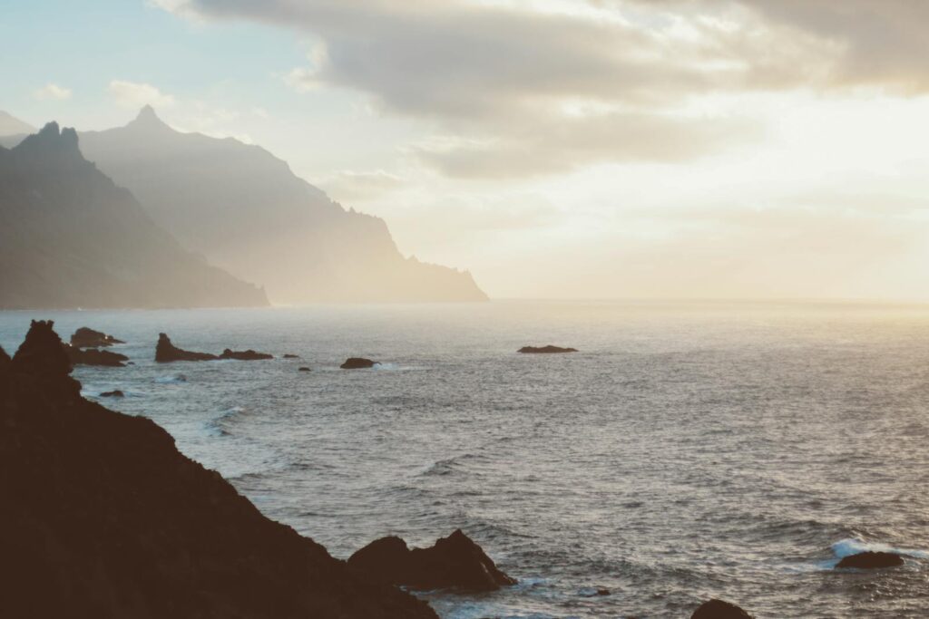 Serene coastal view of misty mountains and ocean at sunrise, captured in Tenerife.