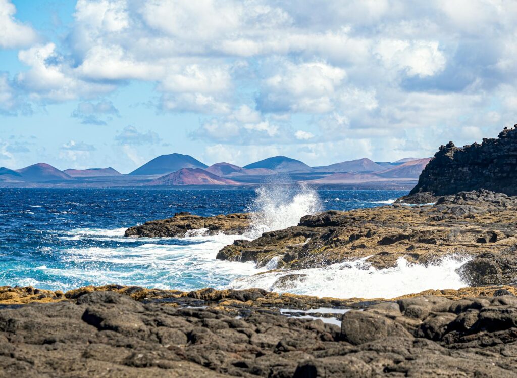 A rugged rocky coastline with waves crashing against the shore under a bright sky.