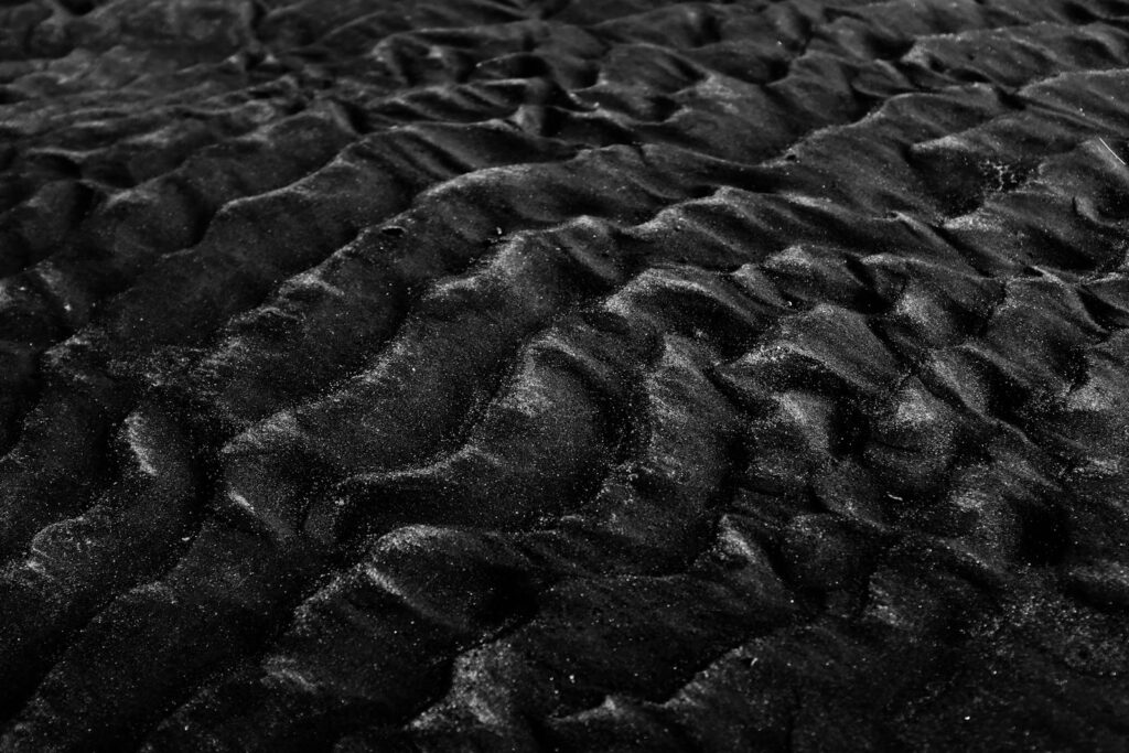 Close-up of textured black sand dunes in monochrome, showcasing natural patterns and textures.