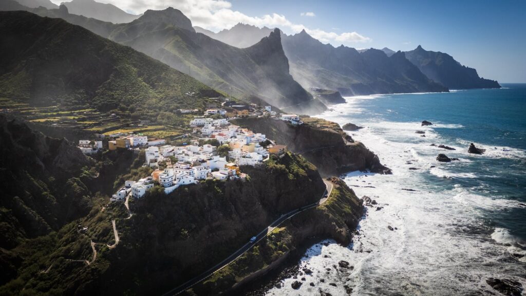 Aerial view of a picturesque coastal village on Tenerife, Canary Islands, with rugged mountains and ocean waves.