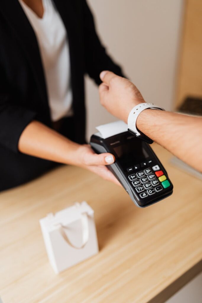 A person using a smartwatch for contactless payment at a store counter with a POS terminal.