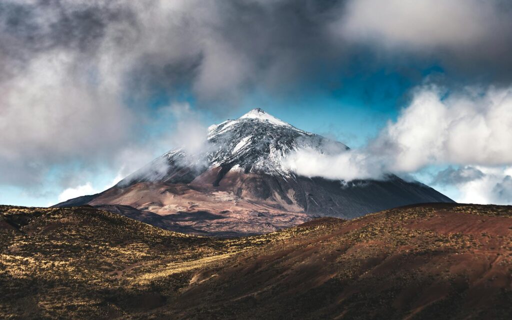 Breathtaking view of Mount Teide with snow-capped peak and drifting clouds in Tenerife, Canary Islands.