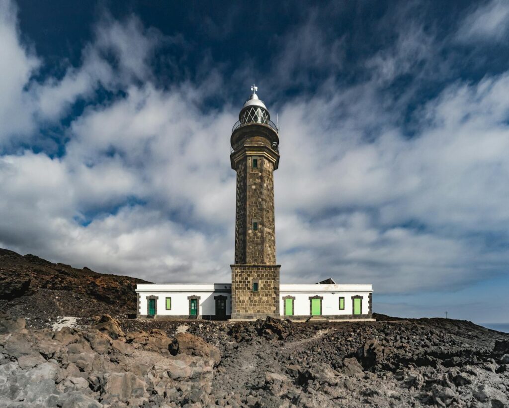 A striking view of the Punta Orchilla Lighthouse against a dramatic volcanic backdrop in Spain, showcasing architectural beauty.