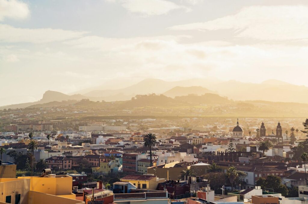 Scenic view of La Laguna cityscape in Tenerife with mountains in the background and a warm sunset glow.