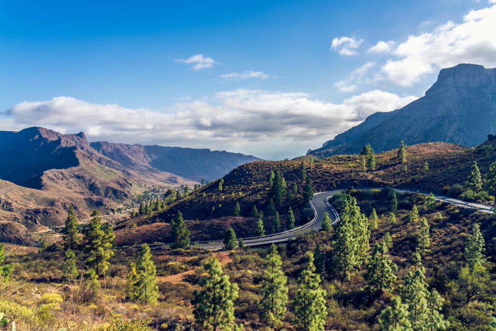 Aerial view of a winding road through a lush mountainous landscape under a clear blue sky.