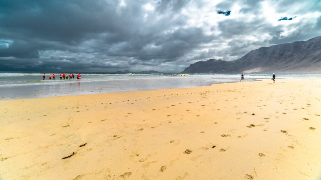 Dramatic cloudy skies over the sandy coast of Lanzarote with people enjoying the beach.