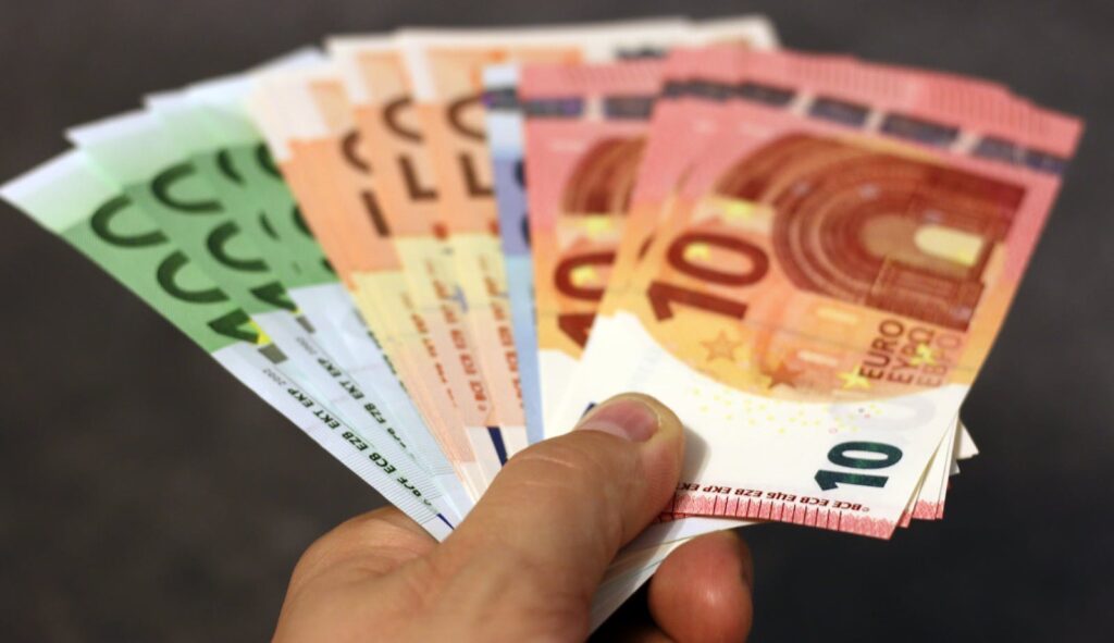 A fan of euro banknotes in various denominations held in a hand.