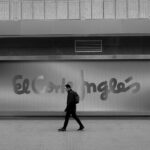 A man walks past El Corte Inglés sign in a monochrome city environment.