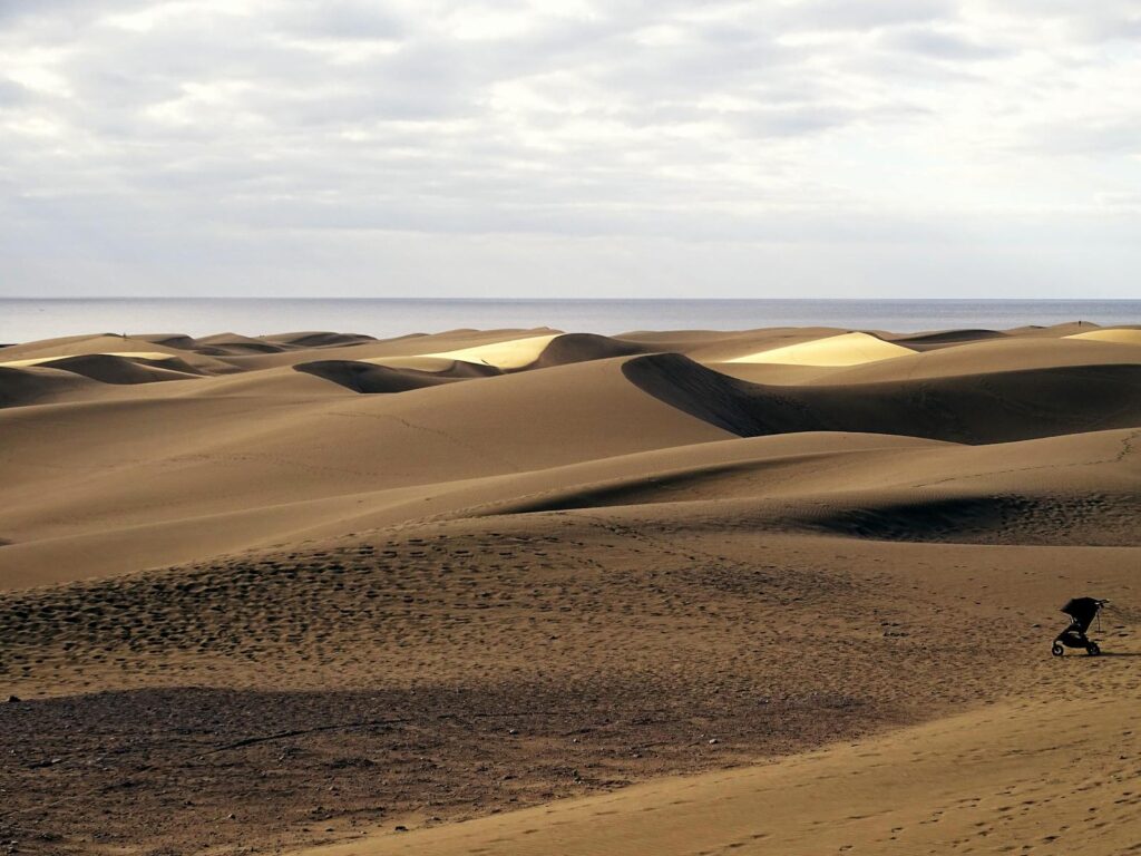 Capture the serene beauty of Maspalomas dunes under a cloudy sky. Ideal for nature lovers and travel enthusiasts.